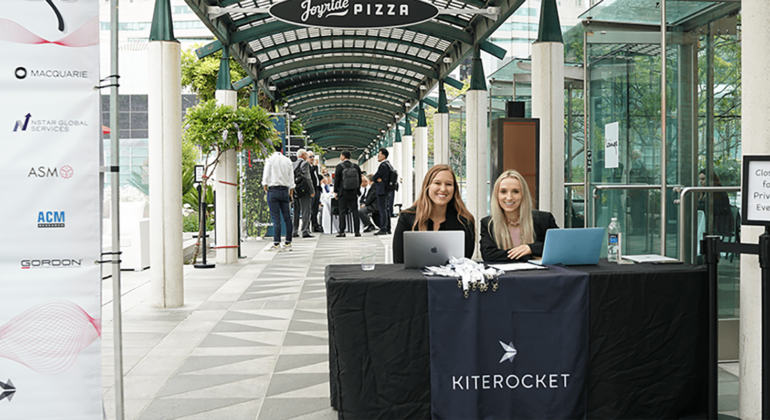 Two KR employees sit at a table in front of the Kiterocket Lounge at SEMICON West 2022