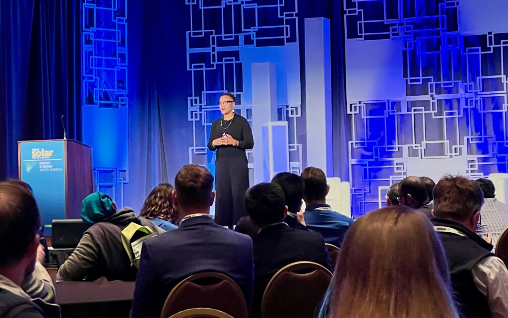 keynote speaker at an event on stage with geometric blue background 